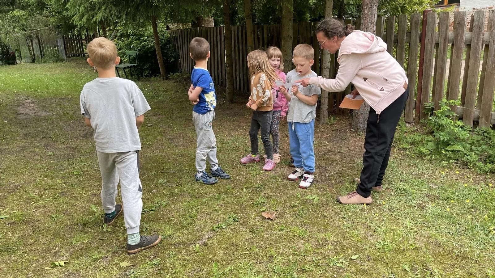 Prowadząca objaśnia zadanie dzieciom podczas zajęć ruchowych na dworze.